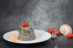 Rice dish mimicking seafood and black ink of squid, served on a plate with apple and tomato. In the background tomatoes and a mussel. The gray background has room for text. photo