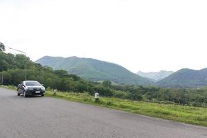 The car is parked on a high road. With mountains and sky in the background photo