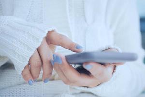 Close up woman hands using smartphone in cold weather background, wearing warm fur knitted clothes photo