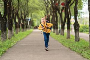 chico con una sudadera amarilla con una mochila en la espalda yendo a la escuela. concepto de regreso a la escuela foto