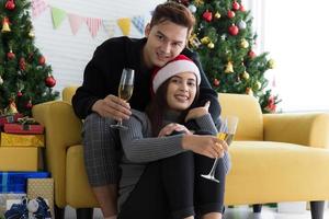 Beautiful young couple is holding glasses of champagne, smiling while celebrating New Year at home photo