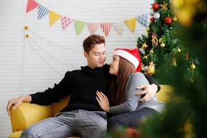 Young happy couple embracing and relaxing on comfortable couch. Lovely couple sitting on sofa and hugging. Beatiful woman and handsome man are affectionate near christmas tree photo