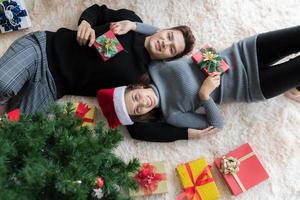 Man and woman lying on carpet on the floor in Christmas decorated room with Christmas tree and gifts box photo