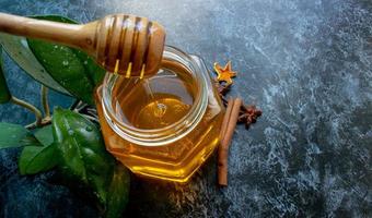 Glass jar with a spoon filled with honey on a black background. Space for your text photo