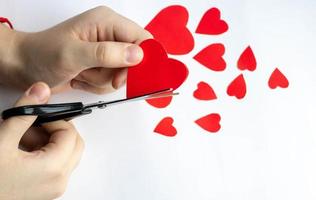 Hands cut out red paper hearts on a white background with scissors. View from above. Valentine's day, mother's day, a symbol of love. Space for copying. photo