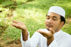 hombre musulmán asiático rezando a alá dios del islam en un prado verde. foto