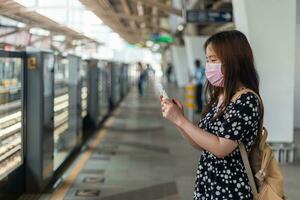 joven mujer asiática pasajera esperando el tren subterráneo cuando escribe un teléfono móvil foto