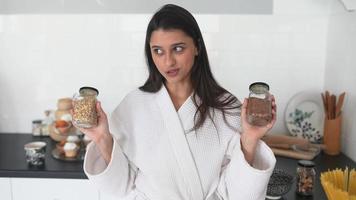 mujer joven en túnica sostiene frascos de condimentos o comida en cocina blanca brillante video