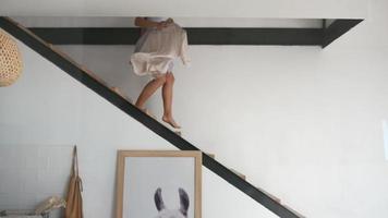 Junge Frau im Sommerkleid läuft die Treppe hinunter und trägt Kleidung auf einem Kleiderbügel video