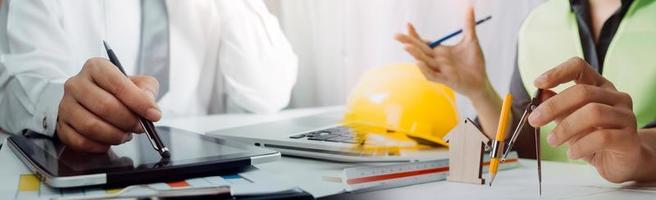 Two colleagues discussing data working and tablet, laptop with on on architectural project at construction site at desk in office photo