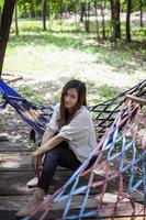 An Asian woman sits in a hammock looking at the camera. photo