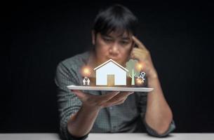 Tablet in hand of a man contemplating buying his first home with a preview of the house displayed above the tablet screen. first home buying idea. selective focus on tablet. photo