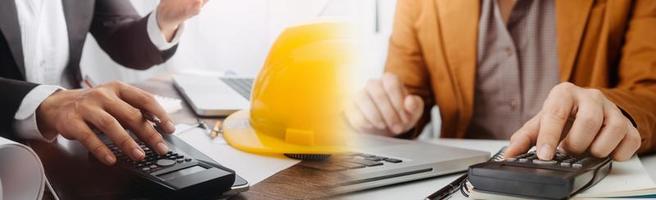 Two colleagues discussing data working and tablet, laptop with on on architectural project at construction site at desk in office photo