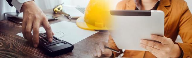 Two colleagues discussing data working and tablet, laptop with on on architectural project at construction site at desk in office photo