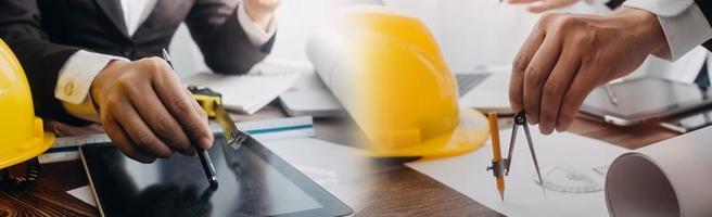 Two colleagues discussing data working and tablet, laptop with on on architectural project at construction site at desk in office photo