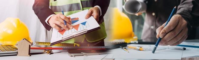 Two colleagues discussing data working and tablet, laptop with on on architectural project at construction site at desk in office photo