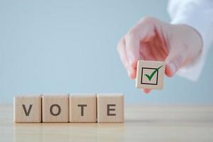 Elections and Voting concept. Hand holding check mark on wooden block with VOTE text on cube blocks photo