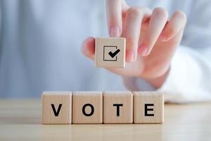 Elections and Voting concept. Hand holding check mark on wooden block with VOTE text on cube blocks photo