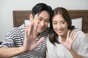 joven pareja asiática sonriente sosteniendo un teléfono inteligente y haciendo videollamadas en casa foto