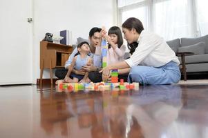 Asian family with children playing and building tower of colorful wooden toy blocks in living room at home, Educational game. photo