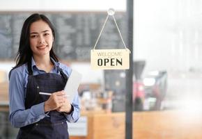 Startup successful small business owner sme beauty girl stand with tablet smartphone in coffee shop restaurant. Portrait of asian tan woman barista cafe owner. SME entrepreneur seller business concept photo