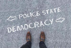 Top view on a man standing in front of the words Police State and Democracy with arrows pointing to the left and right side of the picture photo