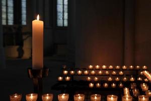 una vela grande y muchas velas pequeñas que iluminan una habitación oscura de la iglesia foto