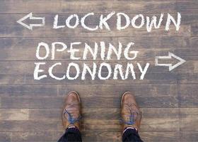 Two leather shoes in front of the words Lockdown and Opening Economy and arrows pointing into opposite directions photo