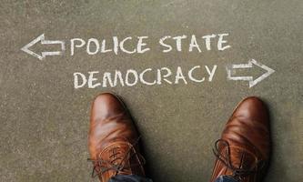 Top view on a man standing in front of the words Police State and Democracy with arrows pointing to the left and right side of the picture photo