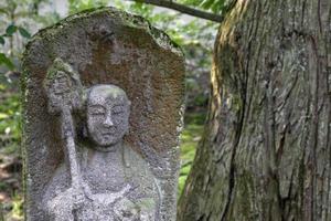 Old weathered monk statue made of stone at Japanese temple photo