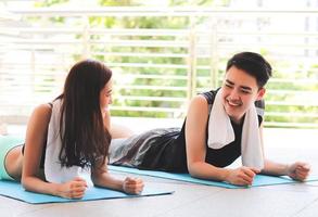 mujer y hombre felices asiáticos con ropa deportiva de yoga, practicando yoga, acostados en una alfombra de yoga, sonriendo y mirándose el uno al otro. fondo de terraza. foto