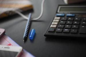 photo of pen and calculator on black wooden table. selective focus.