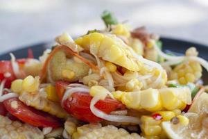 ensalada de maíz de primer plano en plato negro, los tailandeses llaman som tam khow phod. foto