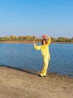 Woman in yellow clothes with red hat posing by the lake in autumn photo