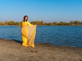 Woman in yellow clothes and a transparent cape posing by the lake. Positive lifestyle photo