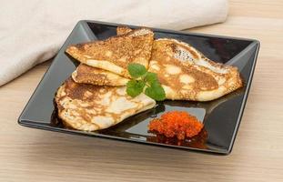 Pancakes with red caviar on the plate and wooden background photo