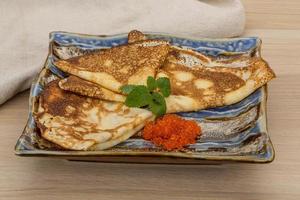 Pancakes with red caviar on the plate and wooden background photo