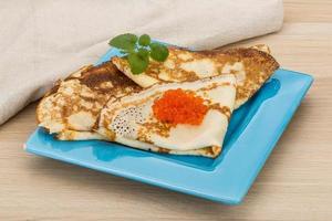 Pancakes with red caviar on the plate and wooden background photo