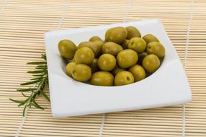 Green olives in a bowl on wooden background photo