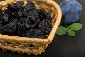 Dried plums in a basket on wooden background photo