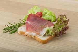 Sándwich de prosciutto sobre tablero de madera y fondo de madera foto