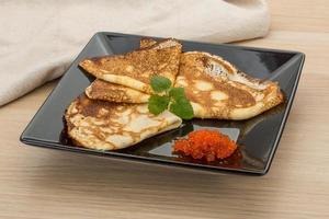 Pancakes with red caviar on the plate and wooden background photo