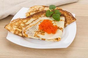 Pancakes with red caviar on the plate and wooden background photo