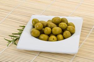 Green olives in a bowl on wooden background photo