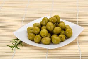 Green olives on the plate and wooden background photo