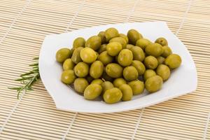 Green olives on the plate and wooden background photo