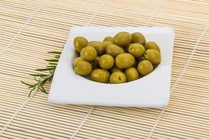 Green olives in a bowl on wooden background photo