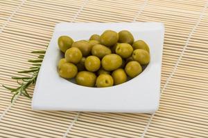 Green olives in a bowl on wooden background photo