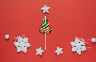 bastón de caramelo en forma de árbol de navidad sobre un fondo rojo. decoraciones navideñas alrededor de una piruleta. feliz Navidad Feliz Año Nuevo foto