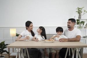 A Healthy Asian Thai family, little children, and young parents drink fresh white milk in glass and bread joy together at a dining table in morning, wellness nutrition home breakfast meal lifestyle. photo